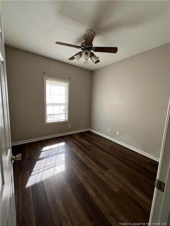 empty room featuring a textured ceiling, ceiling fan, dark wood-type flooring, and baseboards