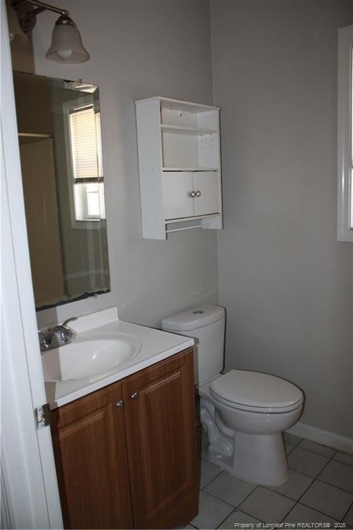 half bath with tile patterned flooring, baseboards, vanity, and toilet