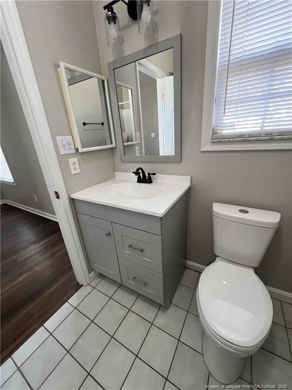 half bath with toilet, tile patterned floors, baseboards, and vanity