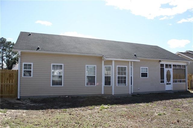 rear view of property featuring a yard, a shingled roof, fence, and a sunroom