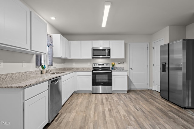 kitchen featuring light wood finished floors, white cabinetry, stainless steel appliances, and light stone counters