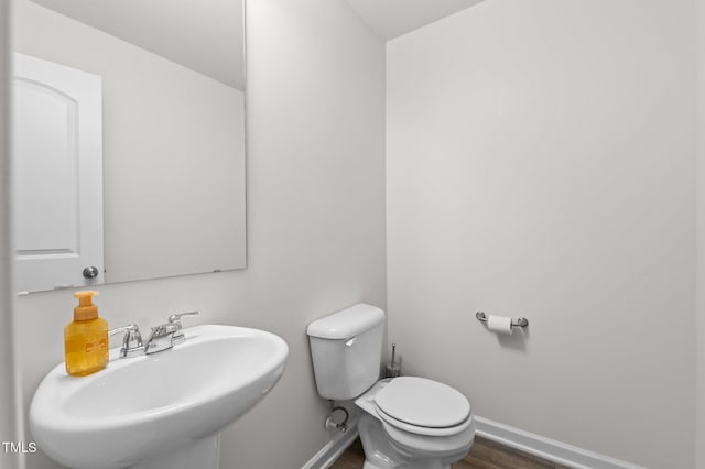 half bathroom featuring toilet, baseboards, a sink, and wood finished floors