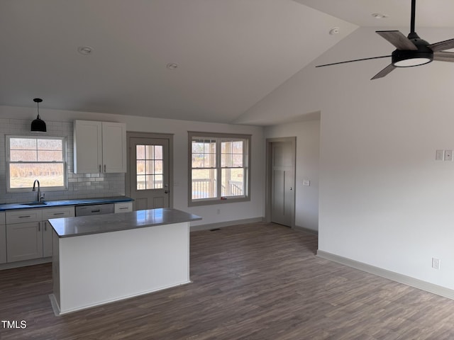 kitchen with baseboards, decorative backsplash, dark wood-type flooring, a center island, and a sink