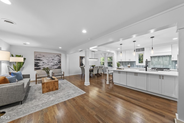 living room featuring dark wood-style flooring, recessed lighting, ornate columns, visible vents, and baseboards