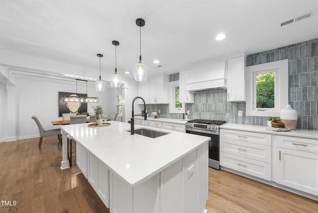 kitchen featuring custom exhaust hood, a wealth of natural light, visible vents, stainless steel range with gas stovetop, and a sink