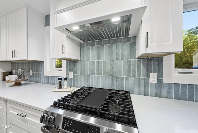 kitchen with stainless steel gas range oven, backsplash, white cabinetry, and under cabinet range hood