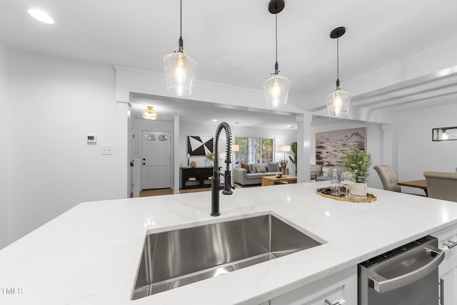 kitchen with pendant lighting, stainless steel dishwasher, ornamental molding, open floor plan, and a sink