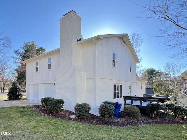 view of home's exterior featuring an attached garage, brick siding, a yard, a chimney, and gravel driveway