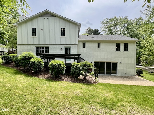 rear view of property featuring brick siding, a yard, a wooden deck, and a patio
