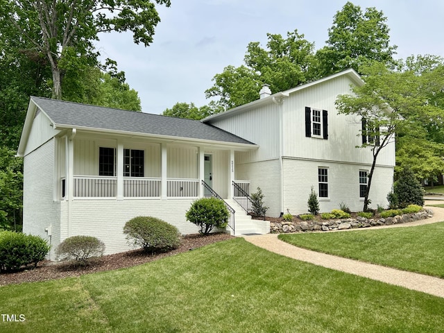 split level home with a chimney, brick siding, a front yard, and roof with shingles