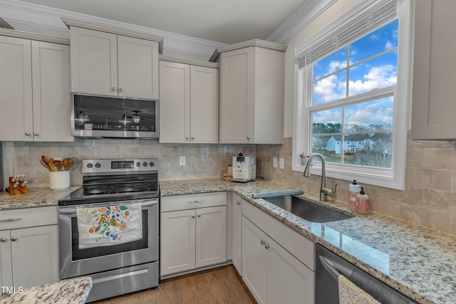 kitchen featuring light stone counters, stainless steel appliances, backsplash, a sink, and wood finished floors