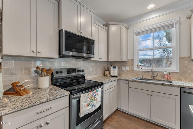 kitchen with wood finished floors, a sink, appliances with stainless steel finishes, ornamental molding, and backsplash