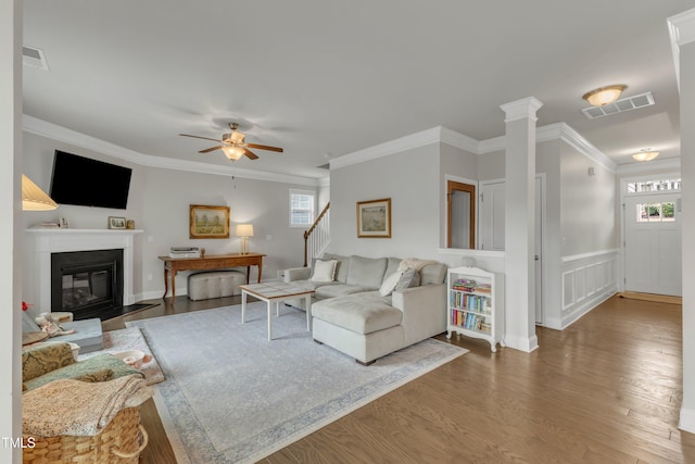 living room with a fireplace with flush hearth, wood finished floors, visible vents, and crown molding