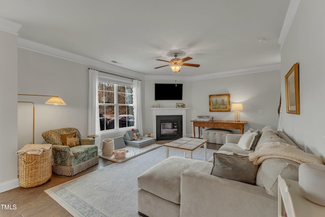 living room featuring ceiling fan, wood finished floors, visible vents, a glass covered fireplace, and crown molding