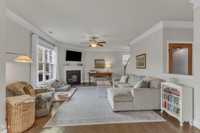 living room featuring a fireplace with flush hearth, wood finished floors, visible vents, and crown molding