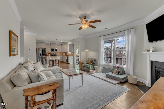 living room with a glass covered fireplace, ceiling fan, wood finished floors, crown molding, and recessed lighting