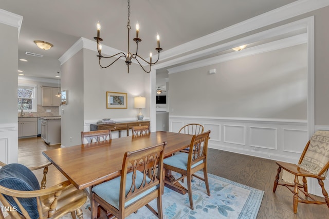 dining area featuring visible vents, a wainscoted wall, ornamental molding, wood finished floors, and an inviting chandelier