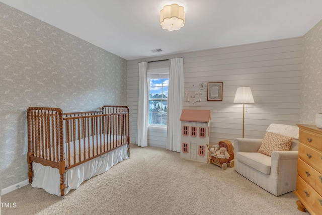 carpeted bedroom with a crib, wallpapered walls, and visible vents