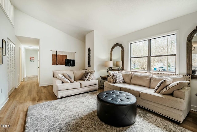 living area with vaulted ceiling, light wood finished floors, and baseboards