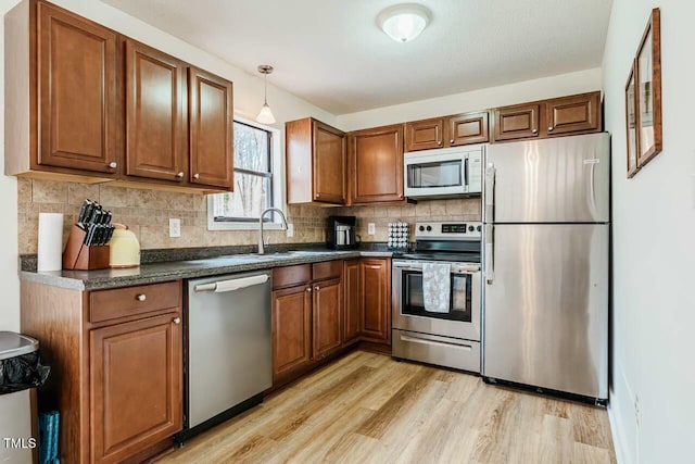 kitchen with brown cabinets, stainless steel appliances, dark countertops, light wood-style flooring, and a sink