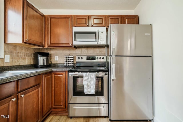 kitchen featuring dark countertops, brown cabinetry, tasteful backsplash, and stainless steel appliances