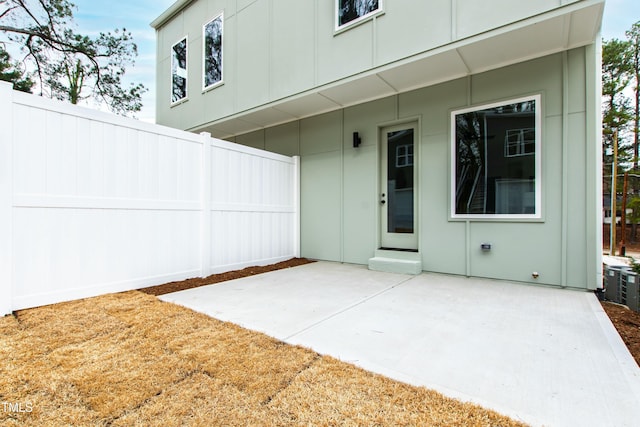 rear view of house featuring board and batten siding, a patio area, and fence