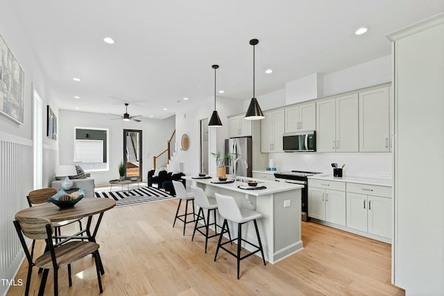 kitchen featuring a center island with sink, stainless steel appliances, light countertops, light wood-style flooring, and a kitchen bar