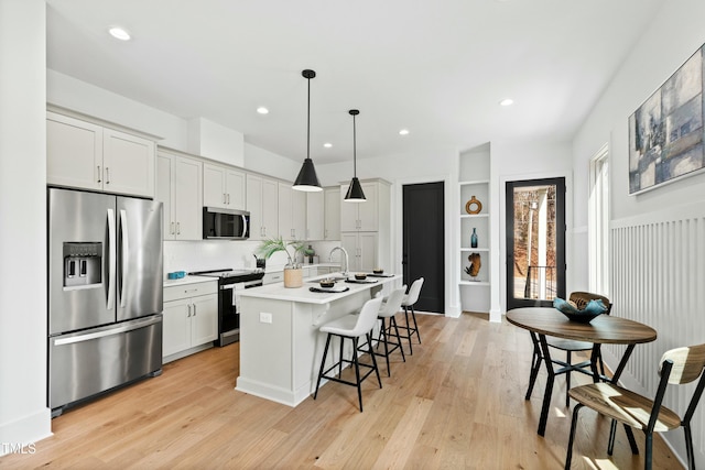 kitchen with stainless steel appliances, a kitchen breakfast bar, light wood finished floors, an island with sink, and decorative light fixtures