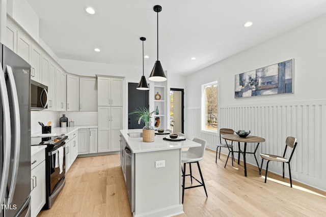 kitchen featuring light wood-style floors, a kitchen bar, stainless steel appliances, and light countertops