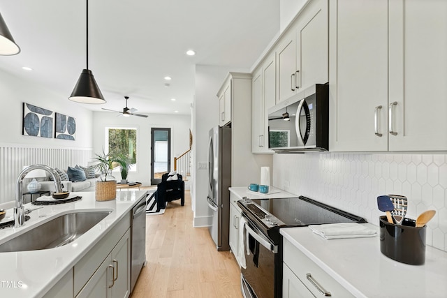 kitchen featuring pendant lighting, light wood finished floors, stainless steel appliances, light countertops, and a sink