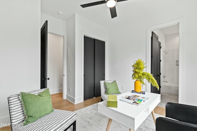 living area with light wood-style floors, baseboards, and a ceiling fan