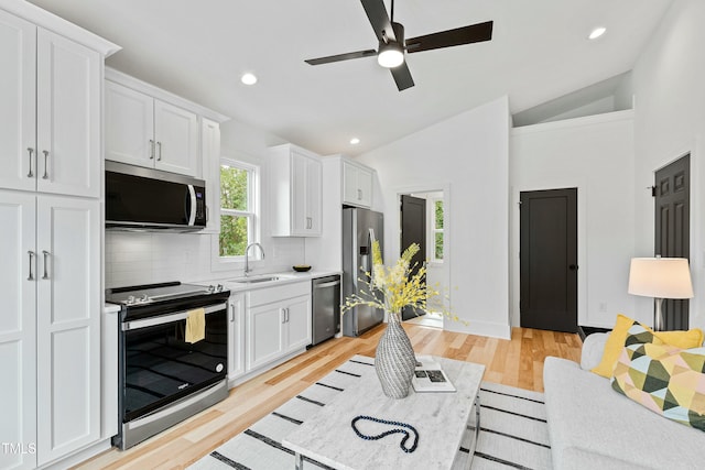 kitchen featuring lofted ceiling, white cabinets, stainless steel appliances, and a sink