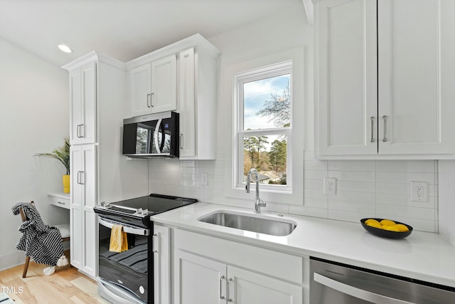 kitchen with stainless steel appliances, a sink, light countertops, and white cabinetry