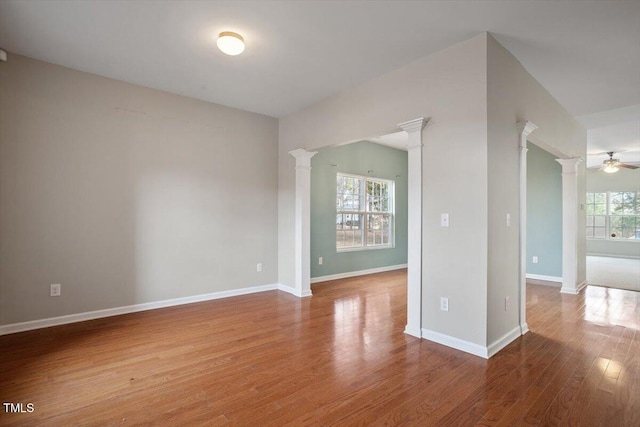 spare room with ceiling fan, decorative columns, baseboards, and wood finished floors