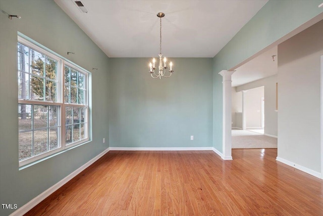 empty room featuring a chandelier, wood finished floors, visible vents, baseboards, and decorative columns