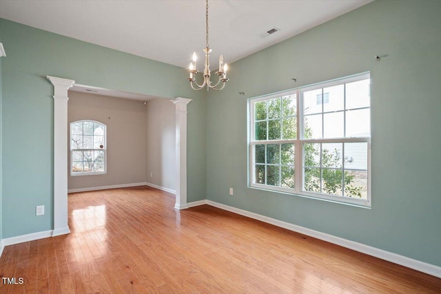 empty room with decorative columns, baseboards, visible vents, wood finished floors, and a notable chandelier