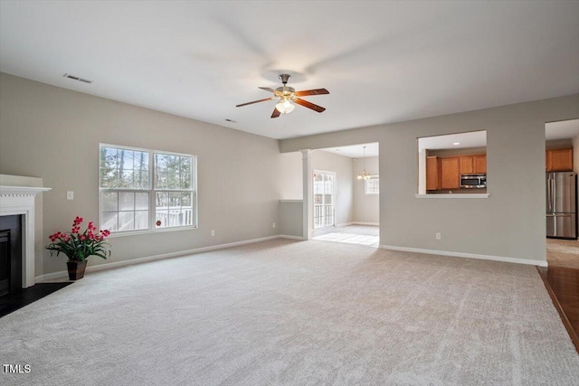 unfurnished living room with light carpet, a fireplace with flush hearth, a ceiling fan, visible vents, and baseboards