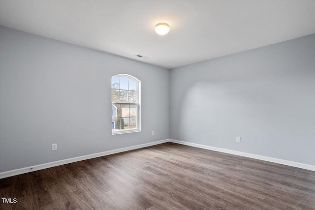 spare room with dark wood-style flooring, visible vents, and baseboards