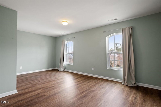 empty room with dark wood-style floors, visible vents, and baseboards