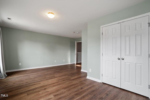 unfurnished bedroom featuring dark wood-type flooring, a closet, visible vents, and baseboards