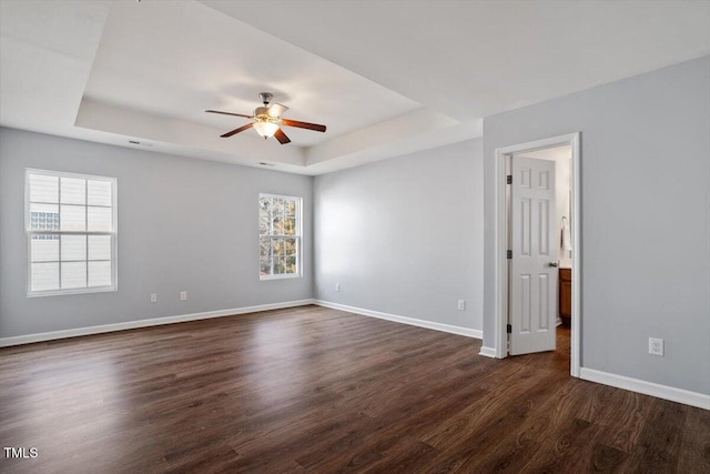 empty room with dark wood-style floors, ceiling fan, baseboards, and a raised ceiling