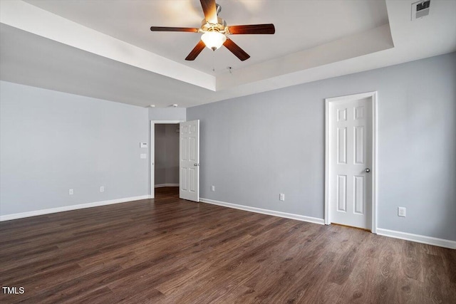 unfurnished room with dark wood-style floors, a tray ceiling, visible vents, and baseboards