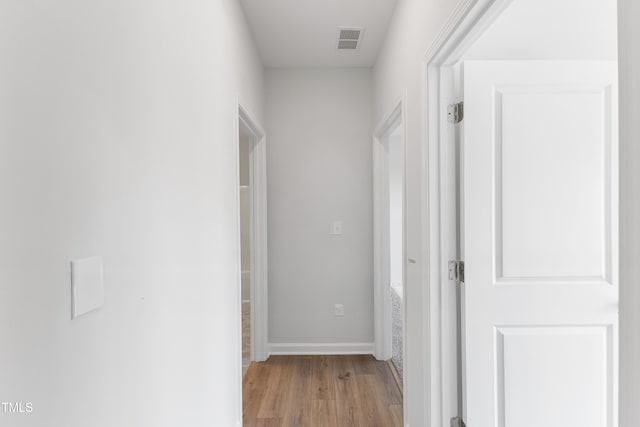 hallway featuring light wood finished floors, baseboards, and visible vents