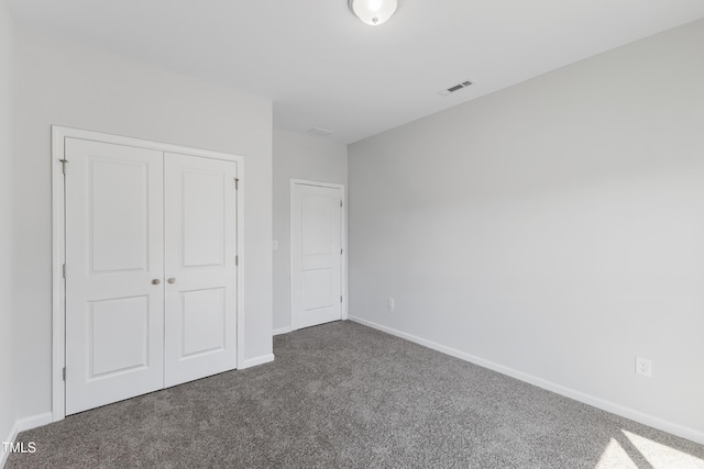 unfurnished bedroom with dark colored carpet, a closet, visible vents, and baseboards