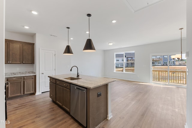 kitchen featuring light stone counters, decorative light fixtures, stainless steel dishwasher, a sink, and light wood-type flooring