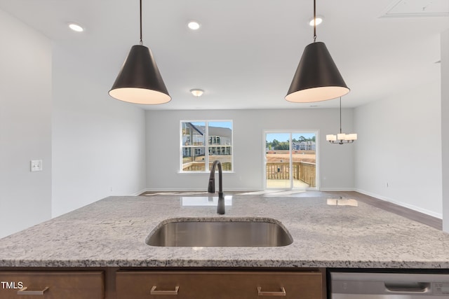 kitchen with light stone counters, pendant lighting, open floor plan, a sink, and dishwasher