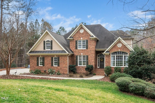 traditional-style house with brick siding, a standing seam roof, a shingled roof, and a front lawn