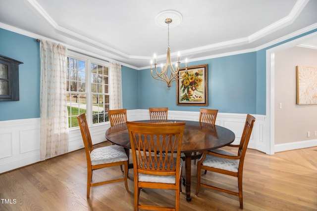 dining space with a raised ceiling, light wood-style flooring, and wainscoting