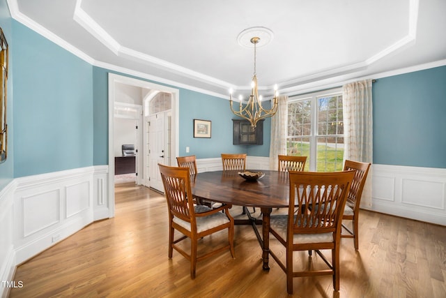 dining space featuring a raised ceiling, light wood-style floors, ornamental molding, and wainscoting