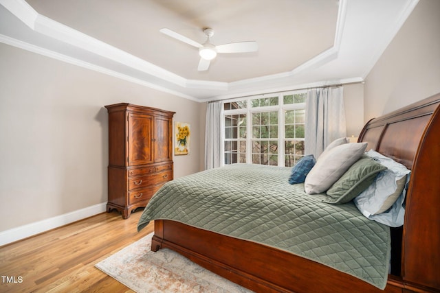 bedroom with light wood finished floors, baseboards, a tray ceiling, ornamental molding, and a ceiling fan